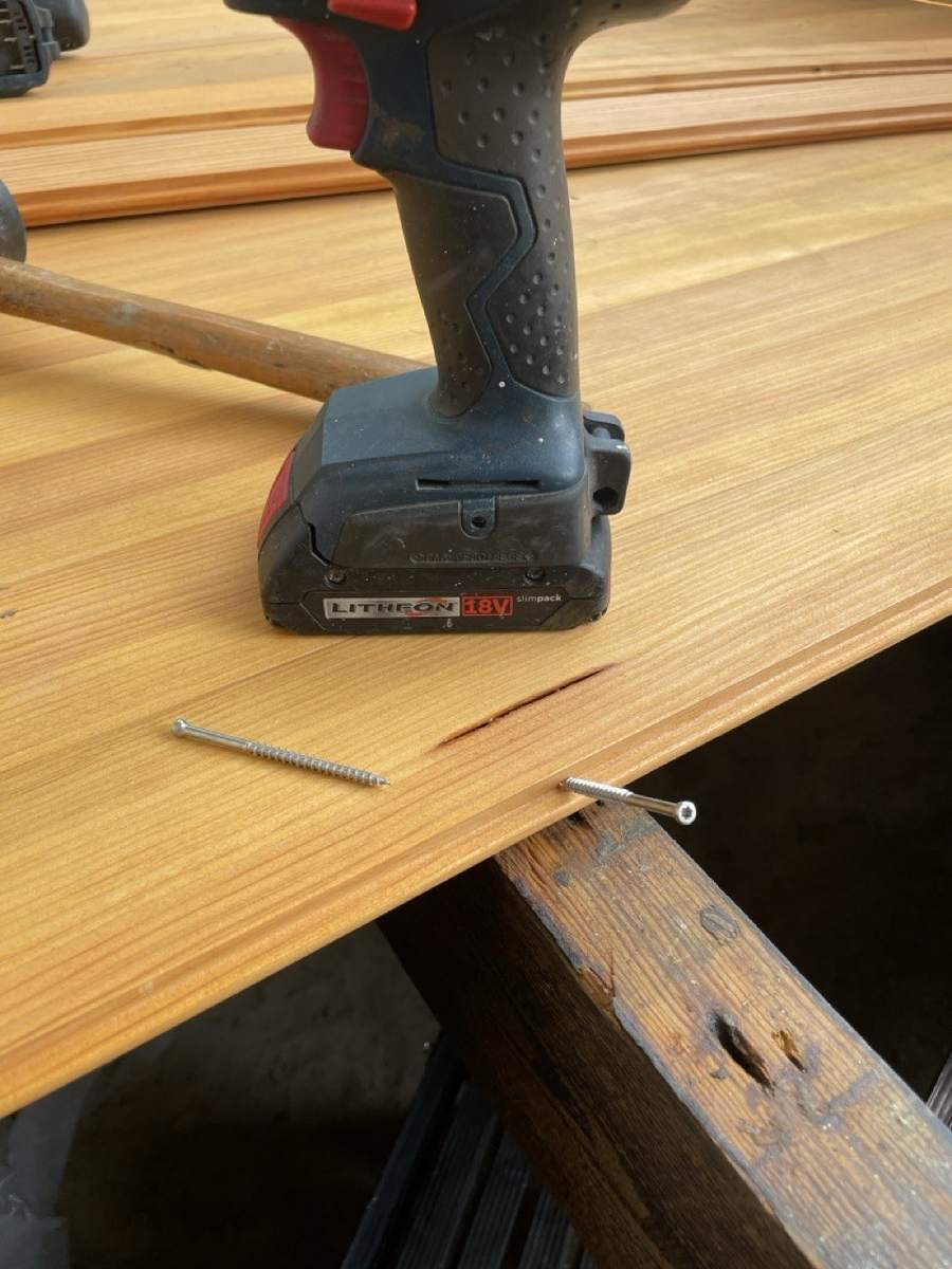 A driver resting on new floorboards with screws set at a board's edge