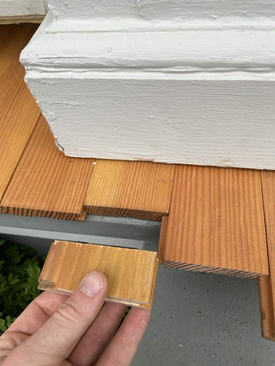 A hand holding a small piece of flooring cut to fit a gap