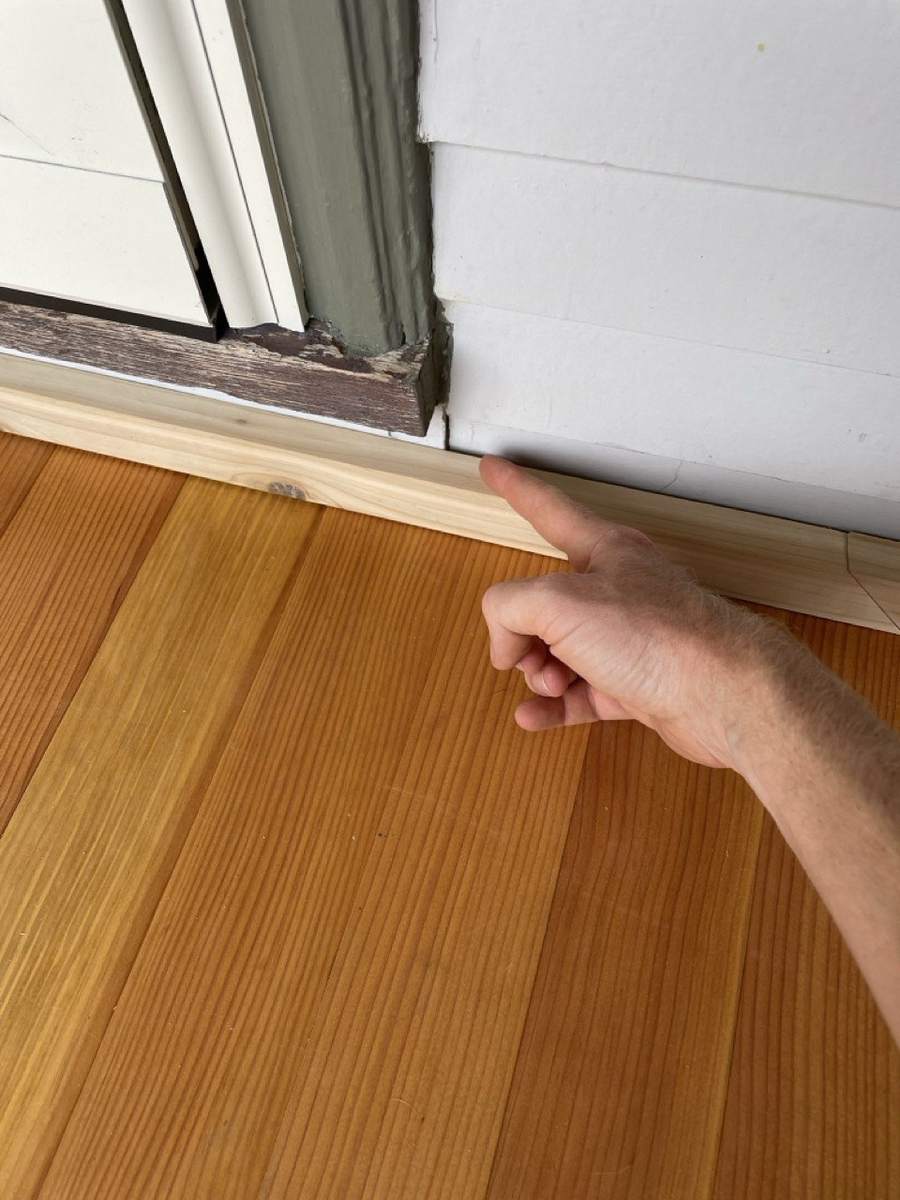 A hand pointing to new trim where the floor meets the wall
