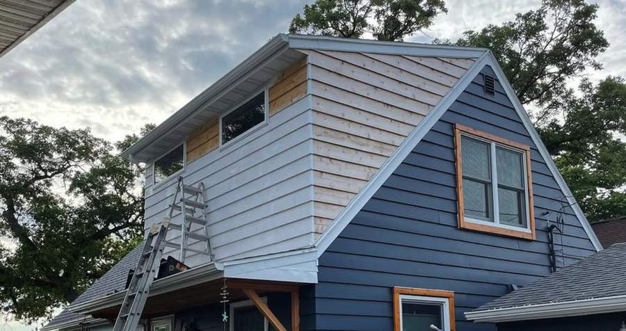 A new dormer on a navy house with fresh siding being primed