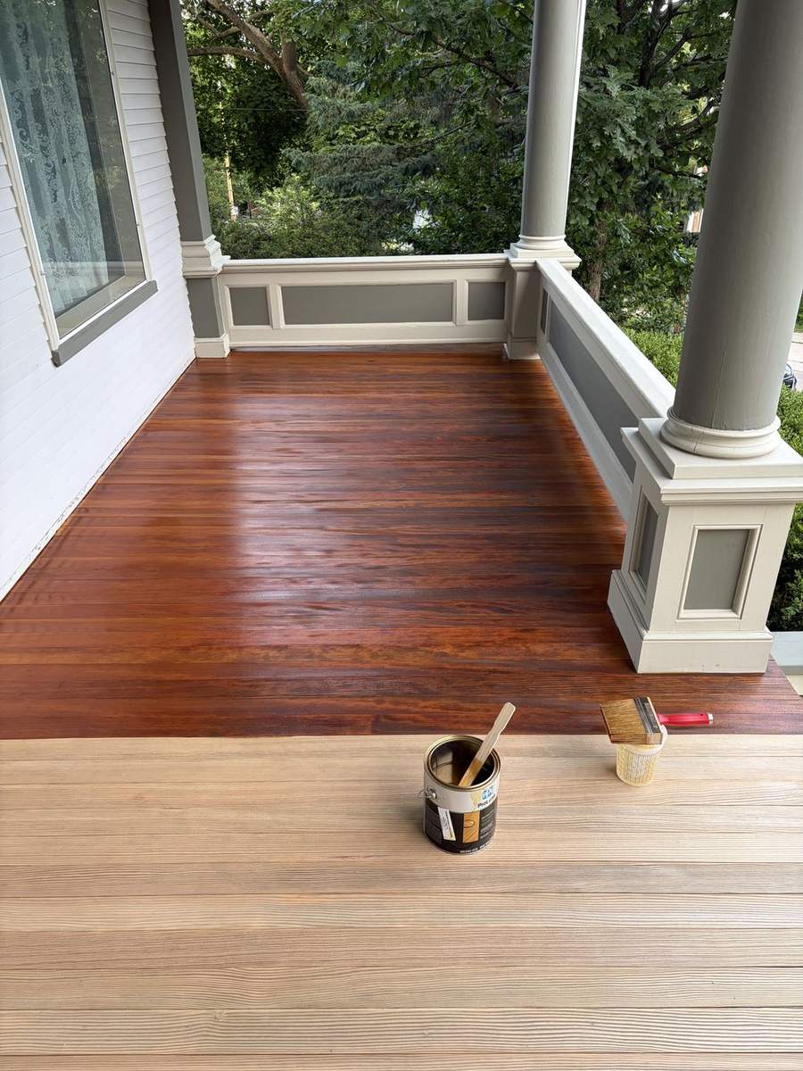A porch floor half stained, with a can of stain on the bare boards