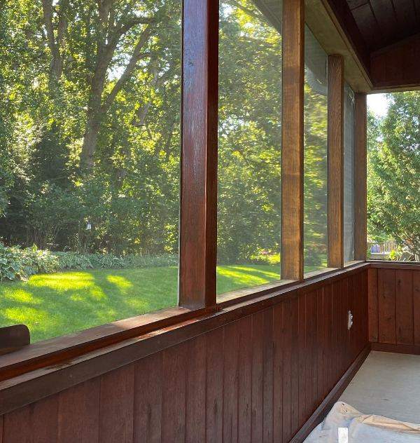 A screened porch with stained wood posts and walls