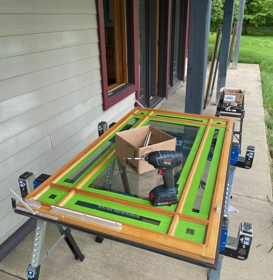 A wood window sash on a workbench with each pane carefully masked